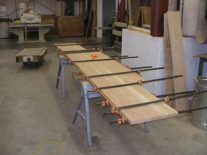 A long cherry desk top clamped together across sawhorses in a workshop