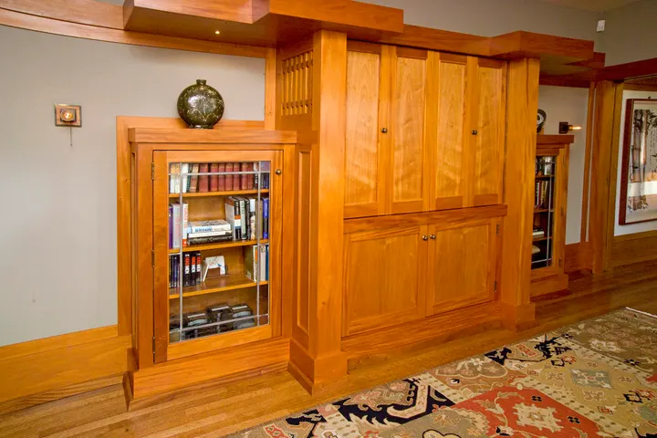A wall of cherry built-in cabinets with a glass-door bookcase on one side and a slatted spindle screen on the other