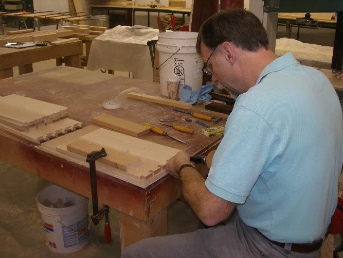 A woodworker at a shop bench cutting dovetail joints, with drawer parts laid out in front of him