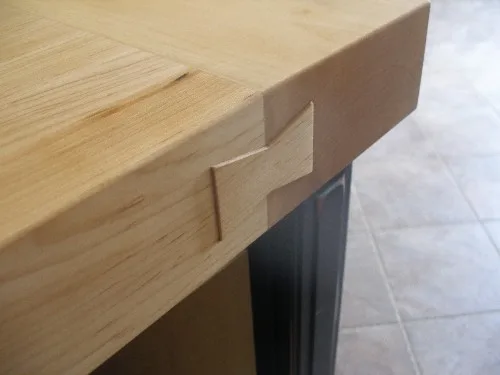 Close-up of a bowtie-shaped maple inlay set across a seam at the edge of a butcher block counter