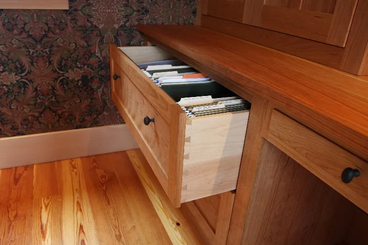 A file drawer pulled open from a cherry desk, showing its pale maple drawer box